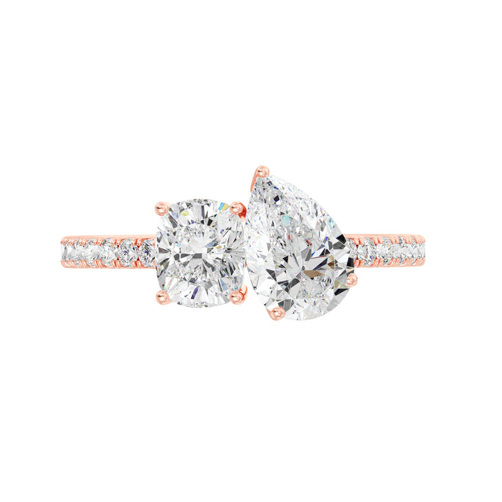 A romantic Pear & Cushion Two-Stone Lab-Grown Diamond 'Toi et Moi' Ring in 18K Rose Gold. Showcasing a 1.00ct Pear-cut diamond and 1.00ct Cushion-cut diamond, set in a delicate prong setting. The ring is further accentuated by 16 Round-Cut Lab-Grown Diamonds (0.24ct total) along the band. The soft blush tones of rose gold complement the brilliance of the diamonds, making it a perfect symbol of love and commitment.