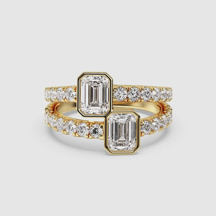 360° view of a Toi et Moi Emerald-Cut Lab-Grown Diamond Ring in 18K Yellow Gold, featuring two bezel-set 1.00ct emerald-cut diamonds and a split shank pavé-set with round lab-grown diamonds. The warm yellow gold setting enhances the brilliance and contrast of the stones, creating a timeless and elegant engagement ring