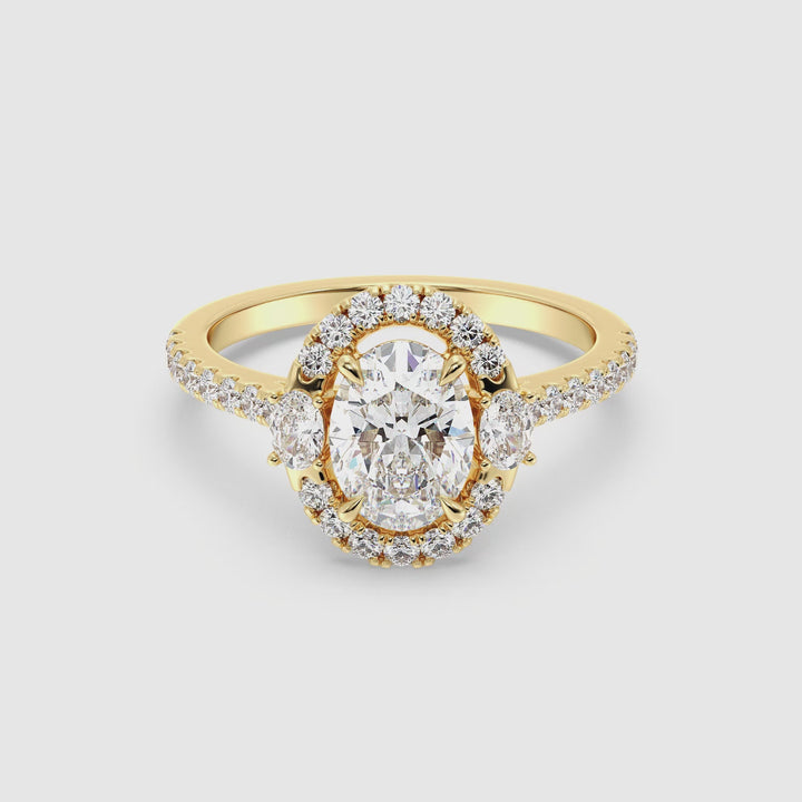 Yellow gold oval lab-grown diamond scallop halo engagement ring featuring a 1.50ct center stone, two side oval diamonds, and pavé-set round diamonds on the shank in a romantic Toi et Moi setting