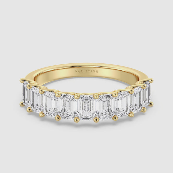 A close-up video of the Lab-Grown Diamond Emerald Scallop Half Eternity Wedding Ring in 18K Yellow Gold. The video showcases the ring's intricate design, highlighting the 9 emerald-cut diamonds set in a low-profile shared prong setting. The camera rotates around the ring, emphasizing the brilliance of the EF/VS lab-grown diamonds and the rich, warm tone of the yellow gold band.