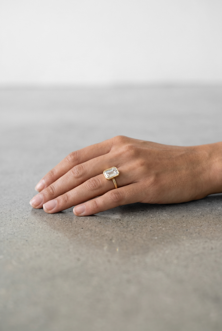 Elegant emerald cut lab grown diamond bezel engagement ring crafted in 18K yellow gold with a sleek contemporary design.