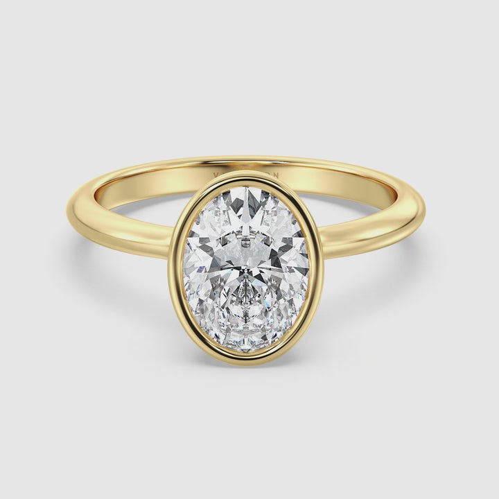 Close-up video of an 18K yellow gold oval-cut lab-grown diamond solitaire ring. The ring features a sleek bezel setting that accentuates the brilliance of the EF/VS diamond. The video showcases the ring from multiple angles, highlighting its elegant design and the radiant sparkle of the diamond