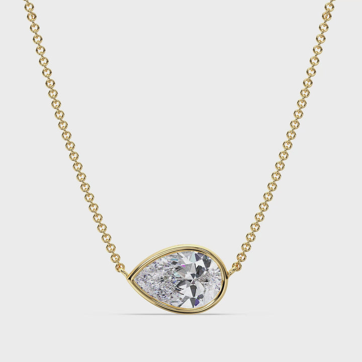 Video showcasing a 2 Carat Lab-Grown Pear-Cut Diamond Bezel-Set Solitaire Pendant Necklace in 18K Yellow Gold. The necklace features a radiant E/VS pear-cut diamond securely set in a sleek bezel design, gracefully suspended on a delicate 18K yellow gold chain. The video captures the brilliance of the diamond, the teardrop shape, and the smooth finish of the gold from various angles.